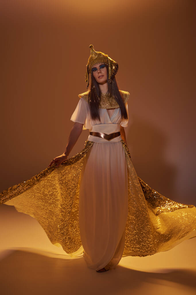Piena lunghezza della donna in abbigliamento egiziano tenendo gonna elegante mentre in piedi su sfondo marrone - Foto, immagini