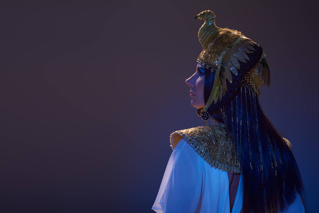 Seitenansicht einer stilvollen Frau mit ägyptischem Kopfschmuck auf braunem Hintergrund mit blauem Licht - Foto, Bild