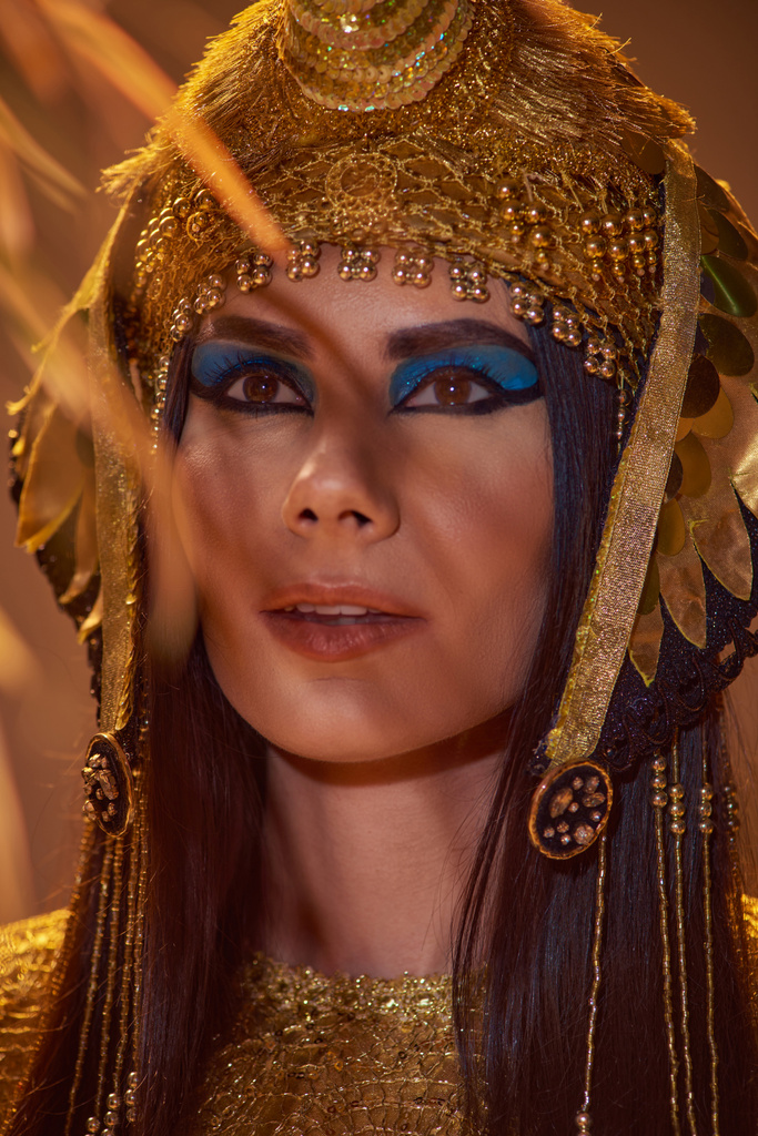 Portrét ženy v elegantní egyptské čelence stojící poblíž pouštní rostliny izolované na hnědé - Fotografie, Obrázek