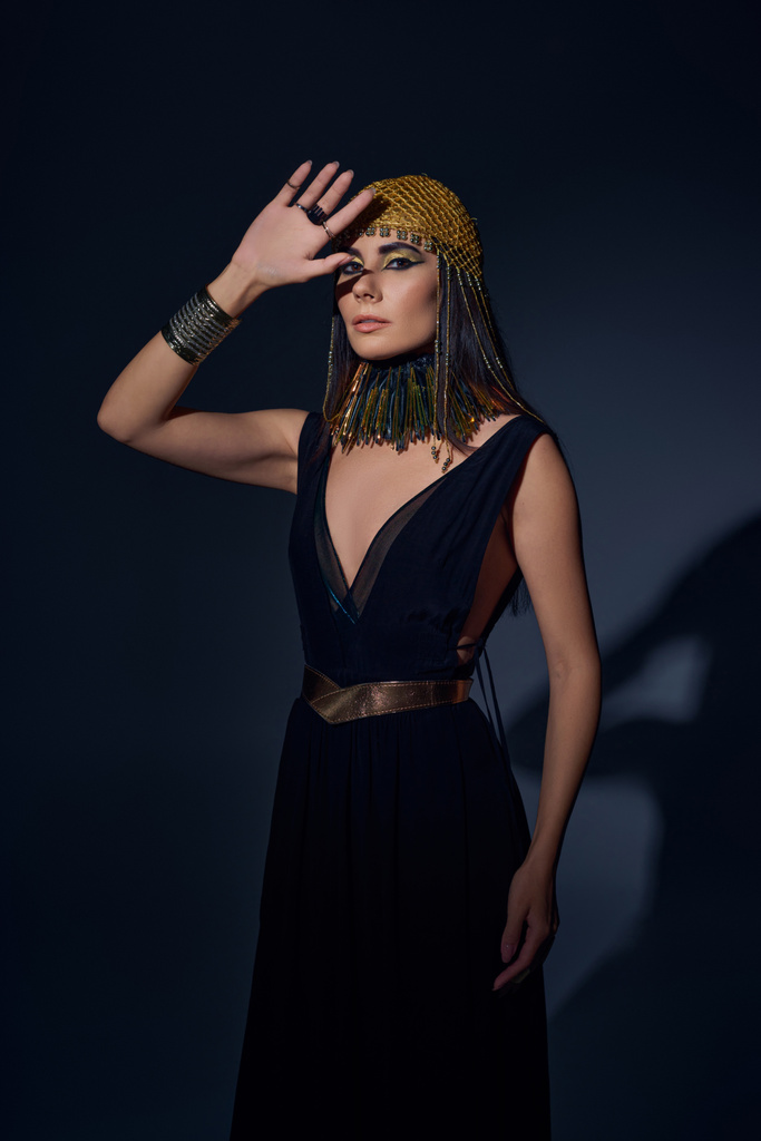 Beautiful woman in egyptian makeup and look posing and looking at camera on blue background - Photo, Image