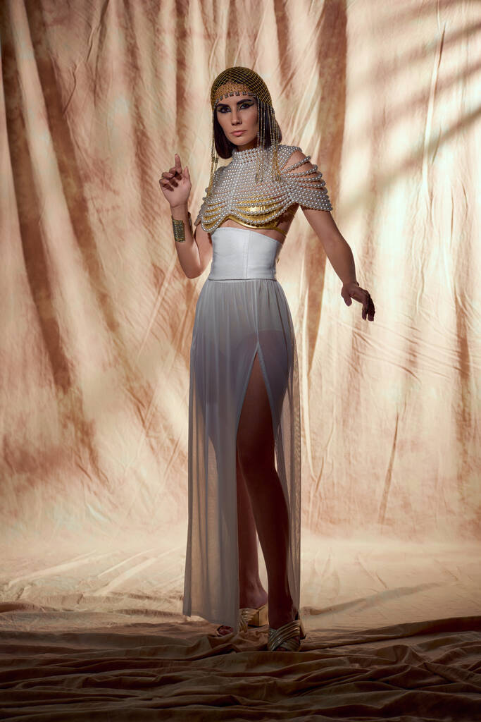 Modelo de moda en atuendo egipcio y la parte superior de perlas posando mientras está de pie sobre fondo abstracto - Foto, imagen
