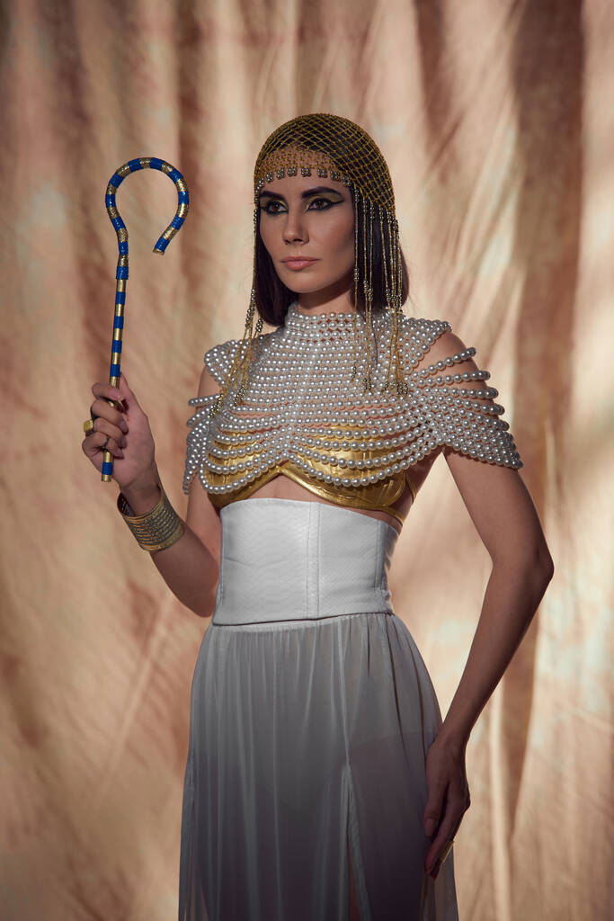 エジプトの外観とパールトップでエレガントな女性 抽象的な背景に伝統的なクロックを保持 - 写真・画像