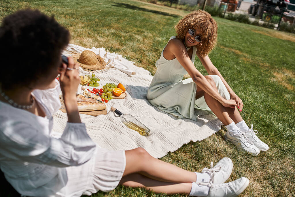 donna afroamericana che scatta foto di fidanzata sulla macchina fotografica vintage, picnic nel parco estivo - Foto, immagini