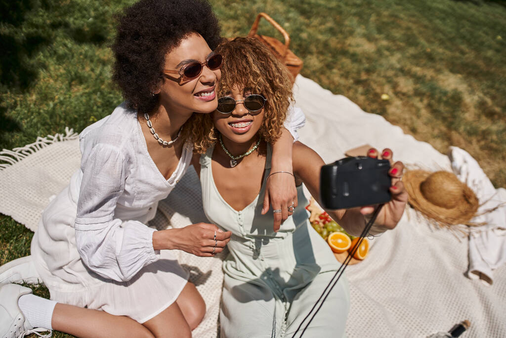 boldog afro-amerikai barátnők ölelés és selfie a vintage kamera, nyári piknik - Fotó, kép