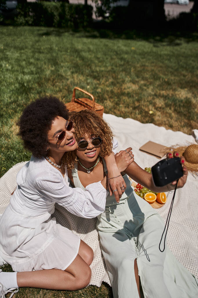 アフリカ系アメリカ人女性,ヴィンテージカメラでセルフィーを取るガールフレンドを抱擁,夏のレジャー - 写真・画像