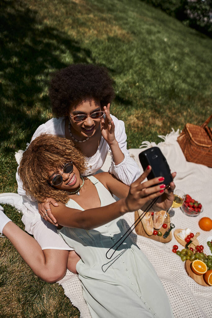 vista superior de namoradas afro-americanas alegres tirando selfie na câmera vintage, piquenique de verão - Foto, Imagem