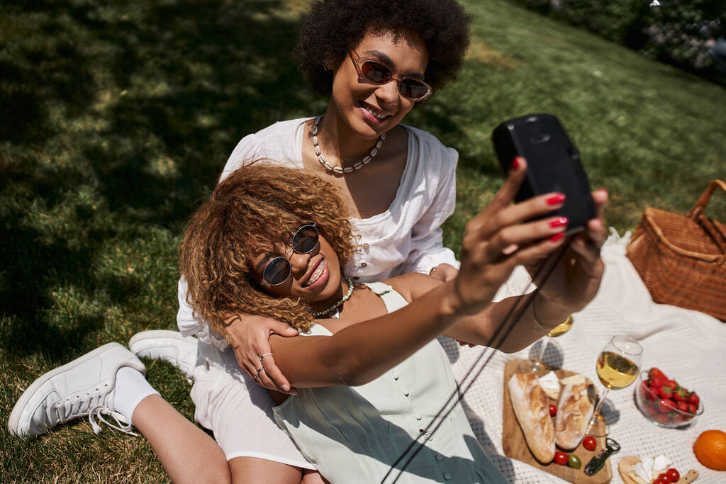 夏の公園でガールフレンドとセルフィーを取るサングラスで陽気なアフリカ系アメリカ人女性 - 写真・画像