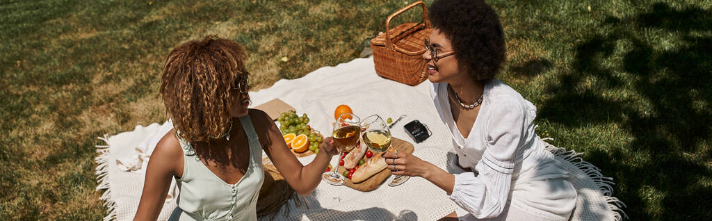 radostné africké americké přítelkyně cinkající sklenice na víno v blízkosti jídla, letní piknik v parku, banner - Fotografie, Obrázek