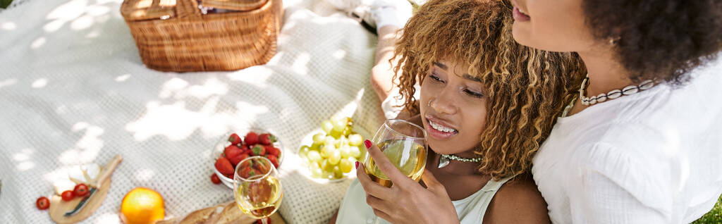 mulher americana africana feliz com copo de vinho perto da namorada e comida em cobertor, lazer verão - Foto, Imagem