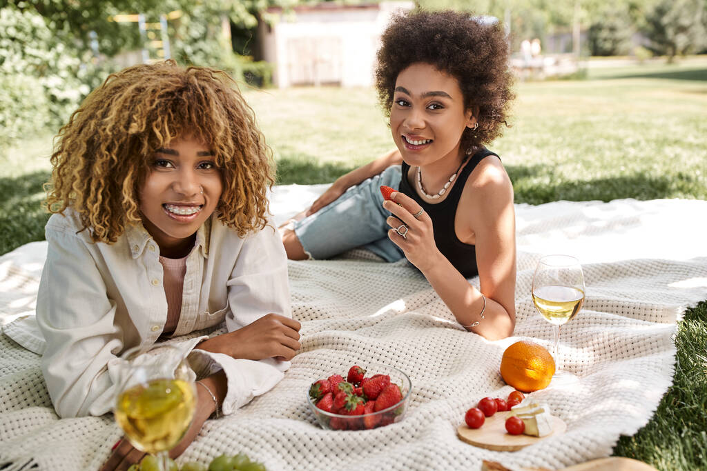 young african american girlfriends smiling at camera near food and wine glasses, summer picnic, park - Photo, Image
