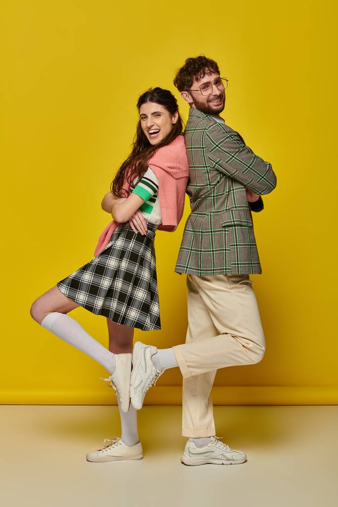 黄色の背景,学生服,若者にポーズバックに立っている幸せなスタイリッシュなカップル - 写真・画像
