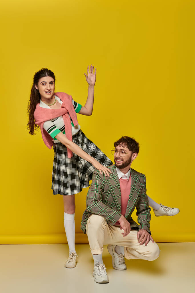 vicces pár, boldog fiatal férfi és nő gesztikulál, pózol sárga háttér, diák ruhák - Fotó, kép