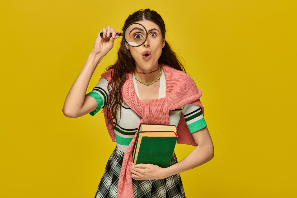 Meraklı genç bir kadın elinde kitap ve büyüteç, yakınlaştırma, keşif, kolej kıyafeti giymiş öğrenci, sarı - Fotoğraf, Görsel