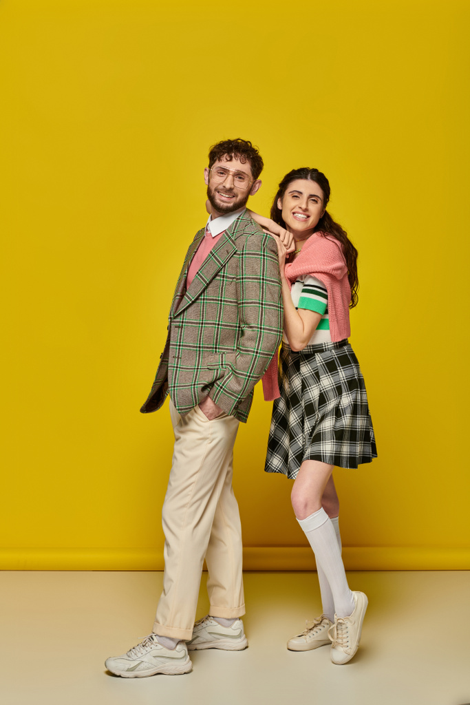 happy students, young woman leaning on man in glasses, college outfits, yellow backdrop, couple - Photo, Image