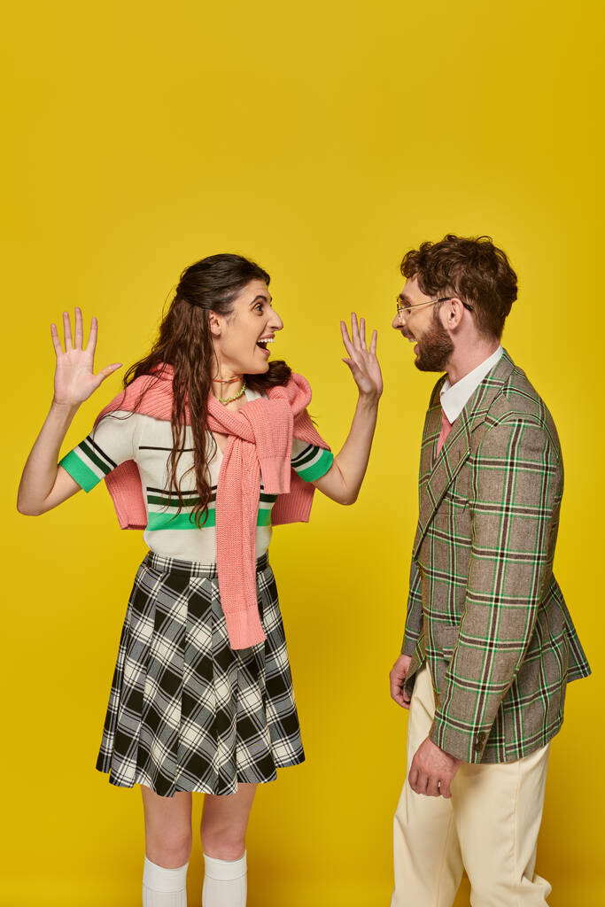 mujer emocionada gesto y mirando al hombre en el fondo amarillo, estudiantes felices, ropa académica - Foto, Imagen