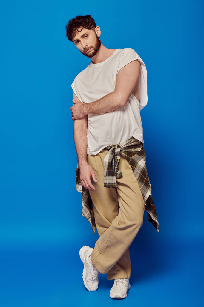 hombre barbudo de pie sobre fondo azul, camiseta y pantalones, zapatillas blancas, moda masculina, estilo - Foto, imagen