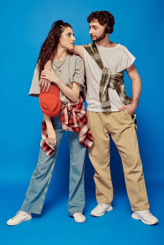 College-Paar, Kopfhörer, Musik, Streetwear, fettes Make-up, Frau mit Baseballkappe, blauer Hintergrund - Foto, Bild