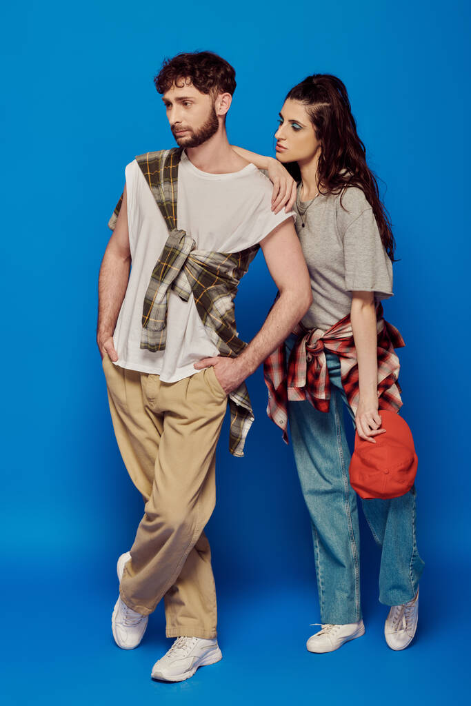 pareja posando en ropa de calle sobre fondo azul, mujer con maquillaje audaz, hombre barbudo, gorra de béisbol - Foto, imagen