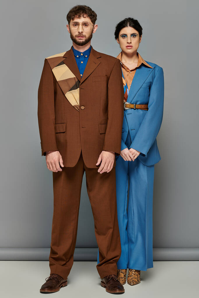 stilvolles Paar posiert in maßgeschneiderten Anzügen, formeller Kleidung, grauem Hintergrund, Mode, blickt in die Kamera - Foto, Bild