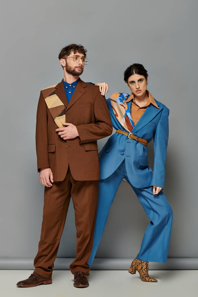 modelos de moda em ternos posando em fundo cinza, homem e mulher elegantes em traje formal sob medida - Foto, Imagem