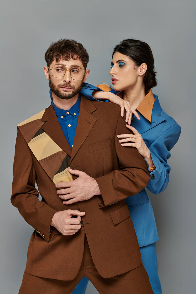 stylowy mężczyzna i kobieta w garniturach pozowanie na szarym tle, elegancki styl, formalne ubranie, wyrafinowane - Zdjęcie, obraz