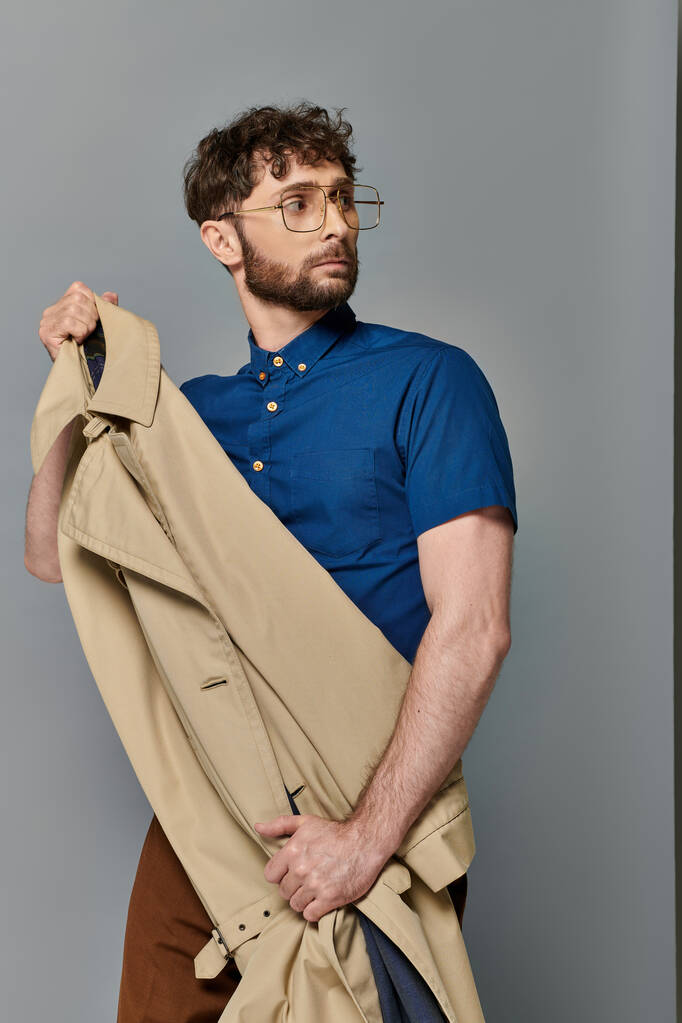 férfi szemüvegben tartó ballonkabát, szürke háttér, stílusos férfi modell néz félre, okos alkalmi - Fotó, kép