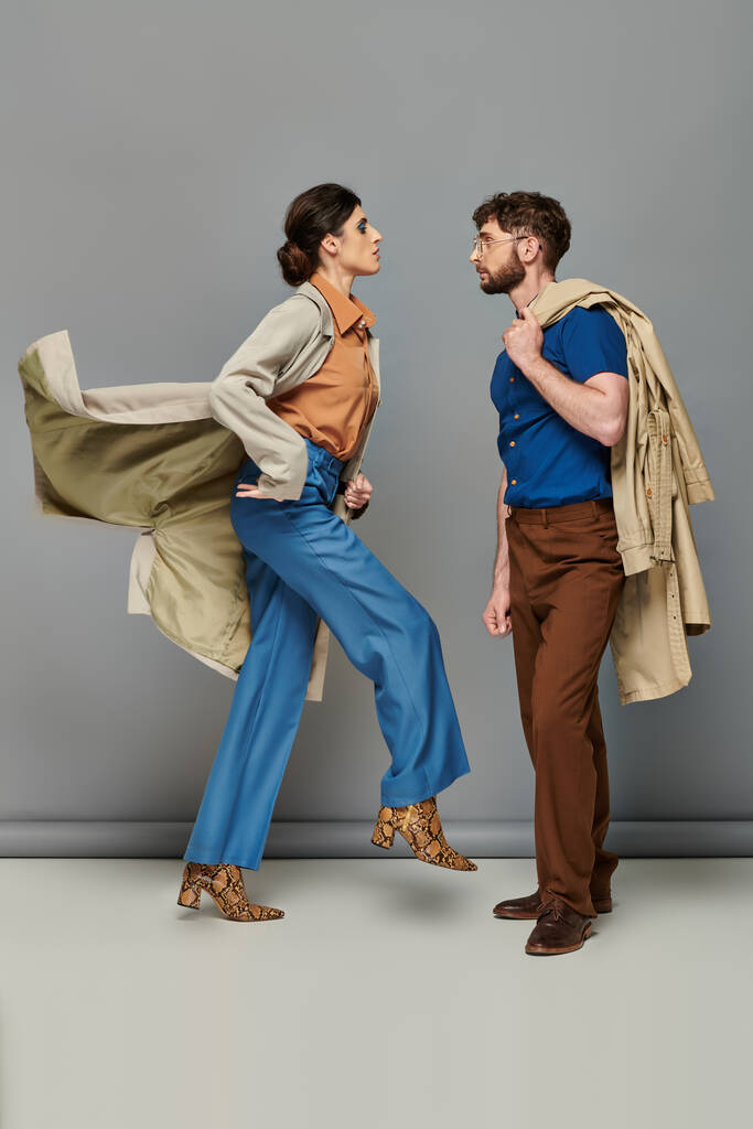 Bewegung, brünette Frau in Animal-Print-Stiefeln, die neben stylischem Mann läuft, graue Kulisse, Oberbekleidung - Foto, Bild