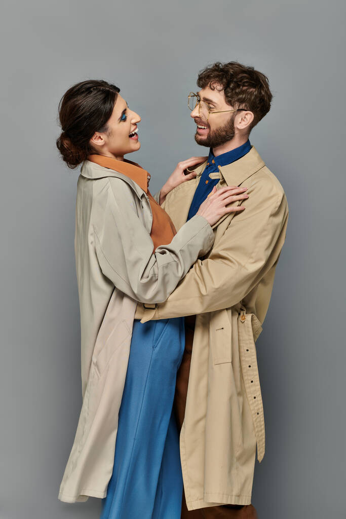 herfst seizoen, gelukkig man en vrouw knuffelen op grijze achtergrond, koppel in trench jassen, stijl, romantiek - Foto, afbeelding