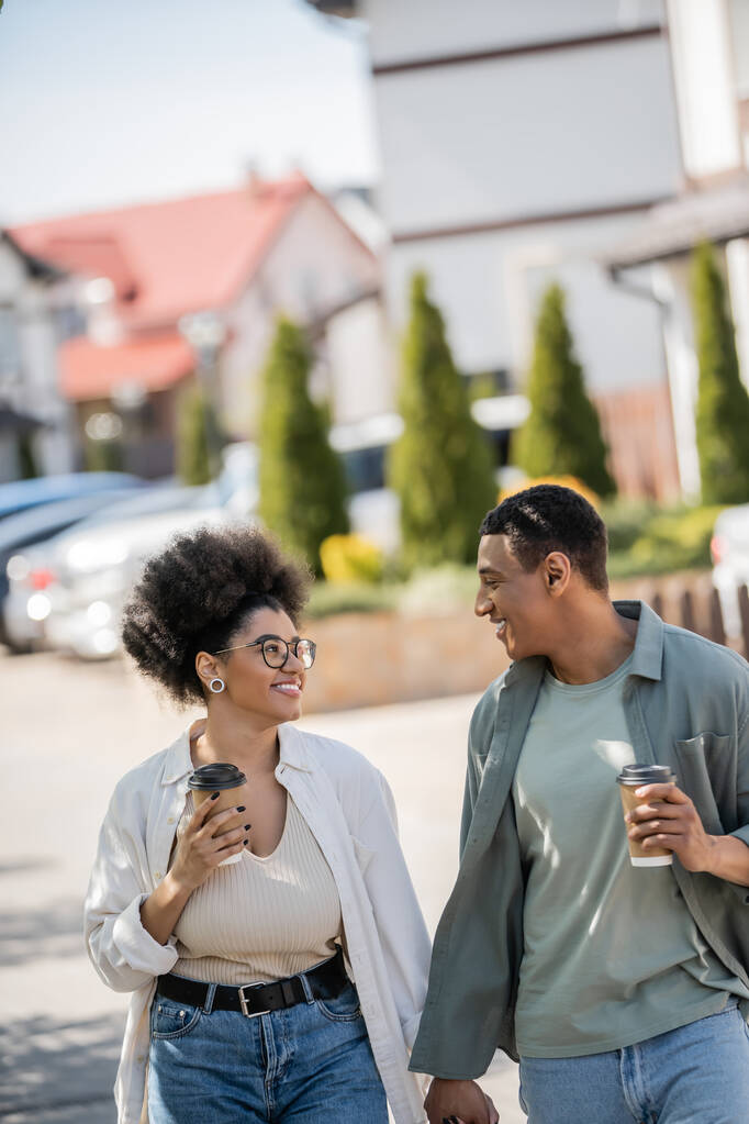 笑顔のアフリカ系アメリカ人のカップルとテイクアウトコーヒーを手に都市の通り - 写真・画像
