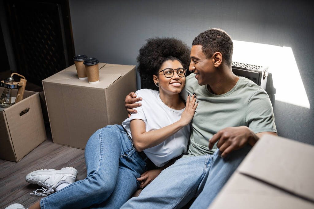 allegra donna afroamericana che abbraccia il fidanzato vicino al caffè per andare e scatole in una nuova casa - Foto, immagini