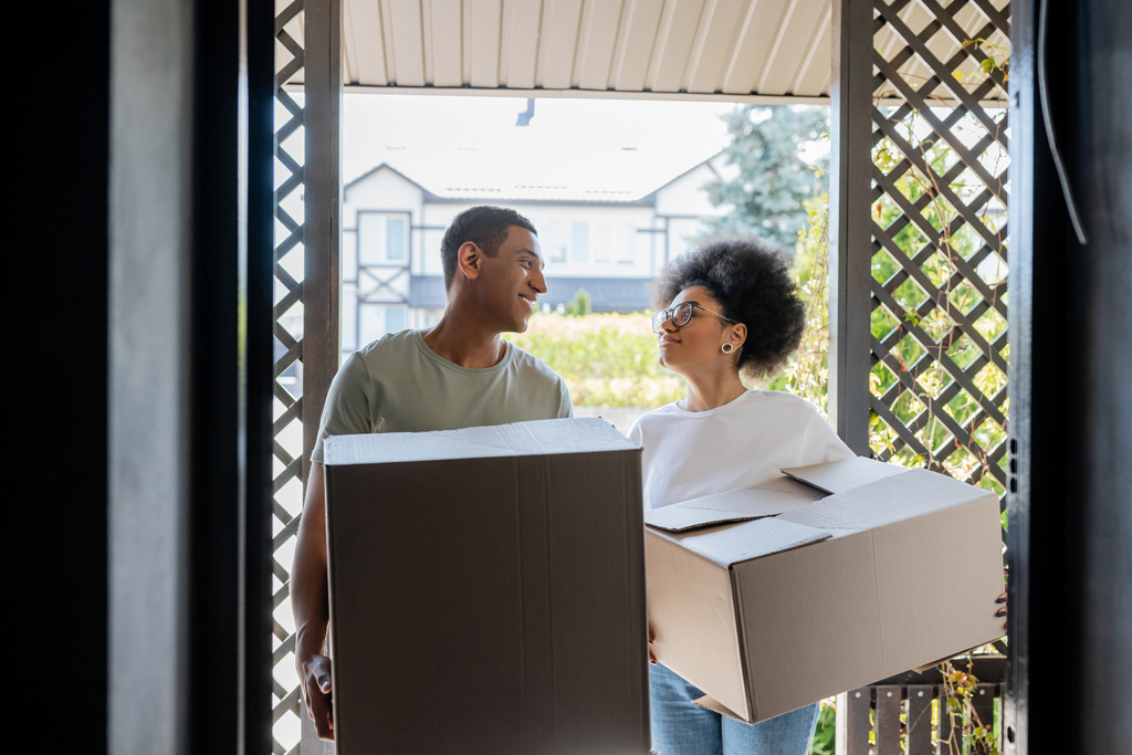 sorridente romântico casal afro-americano segurando caixas de papelão perto da porta da nova casa - Foto, Imagem