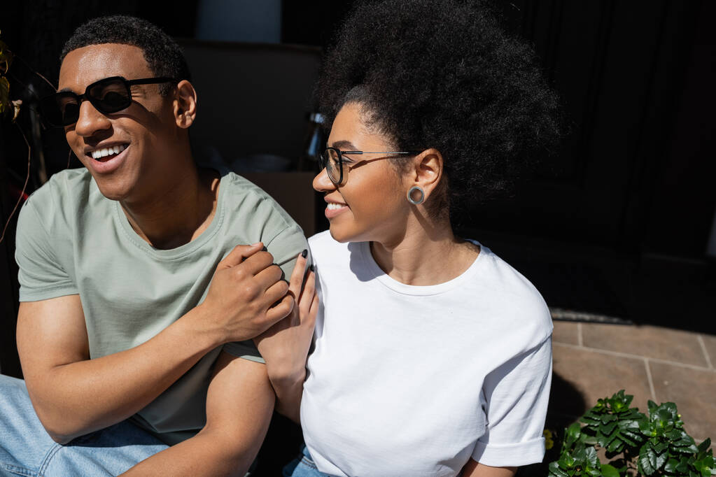smiling african american woman hugging boyfriend in sunglasses on porch of new house - Photo, Image