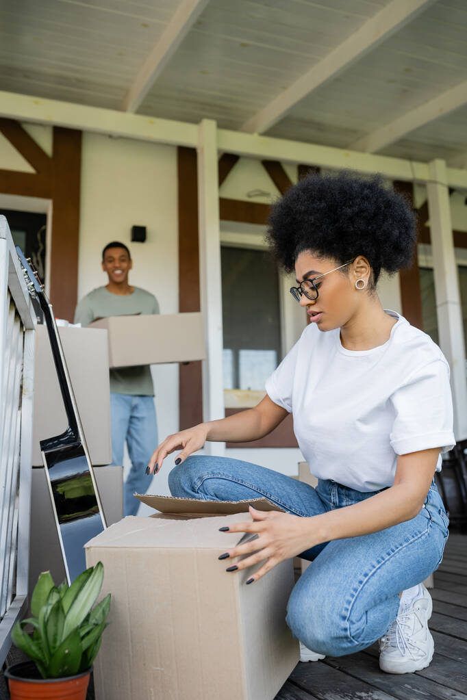 mujer afroamericana desembalaje paquete cerca borrosa novio, cajas y nueva casa - Foto, imagen
