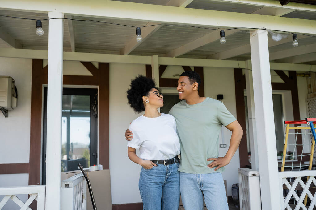 щаслива афро-американська пара обіймається, стоячи на ганку біля нового будинку на відкритому повітрі - Фото, зображення