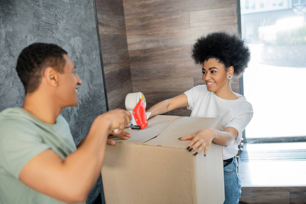 hymyilevä afrikkalainen amerikkalainen nainen tilalla laatikko lähellä poikaystävä teipillä liikkumisen aikana - Valokuva, kuva