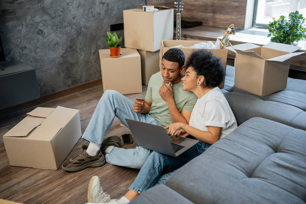 donna afro-americana che parla con fidanzato pensieroso durante lo shopping online vicino a scatole in una nuova casa - Foto, immagini
