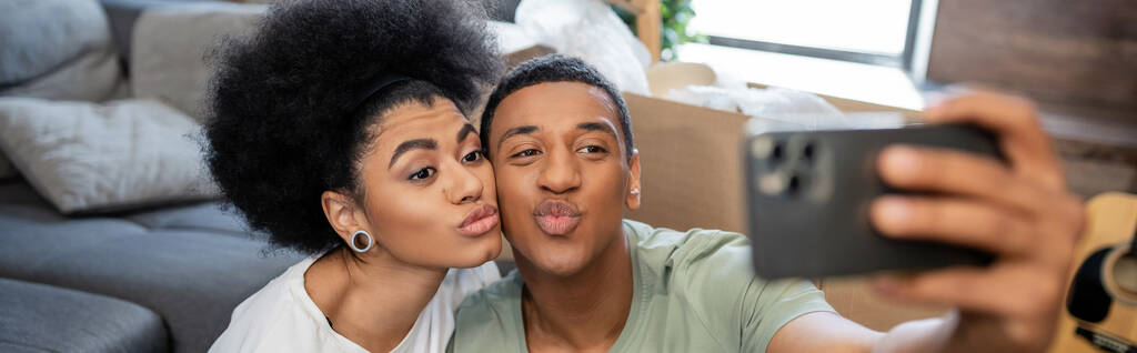 africano americano pareja tomando selfie en smartphone y pucheros labios en nuevo casa, bandera - Foto, imagen