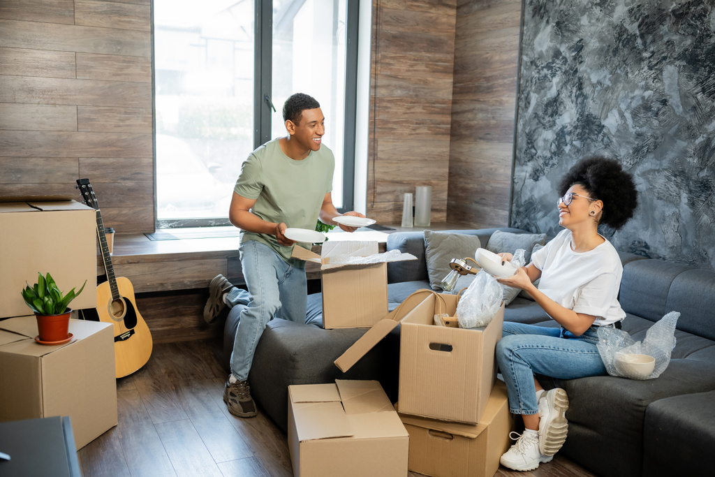 radostný africký americký pár vybalování lepenkové balíčky v novém obývacím pokoji doma - Fotografie, Obrázek