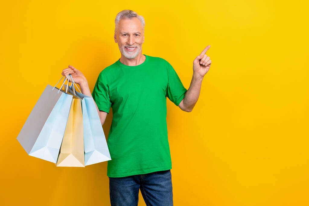 Portrét pohledný muž držet boutique tašky indikují prst prázdný prostor nabídka izolované na žlutém pozadí. - Fotografie, Obrázek