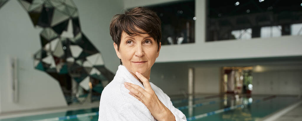 middle aged woman with short hair standing in white robe, spa center, indoors swimming pool, banner - Photo, Image