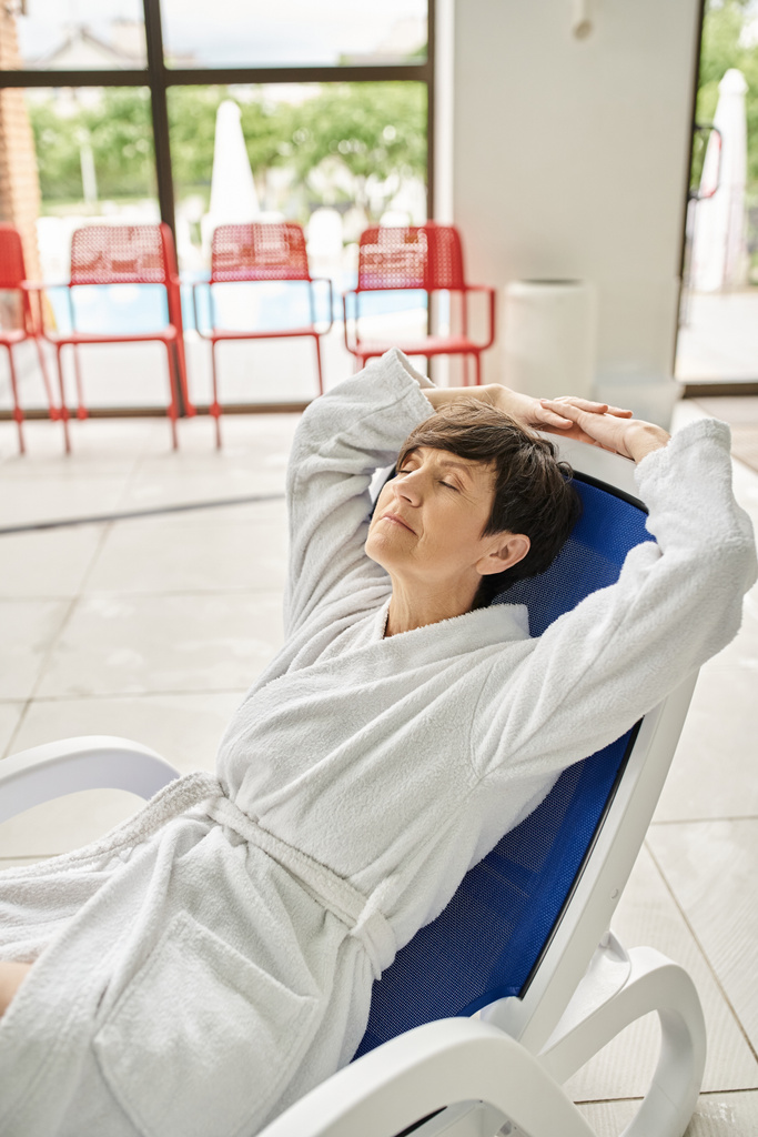 donna di mezza età con capelli corti rilassante sul lettino, accappatoio bianco, centro benessere, occhi chiusi - Foto, immagini