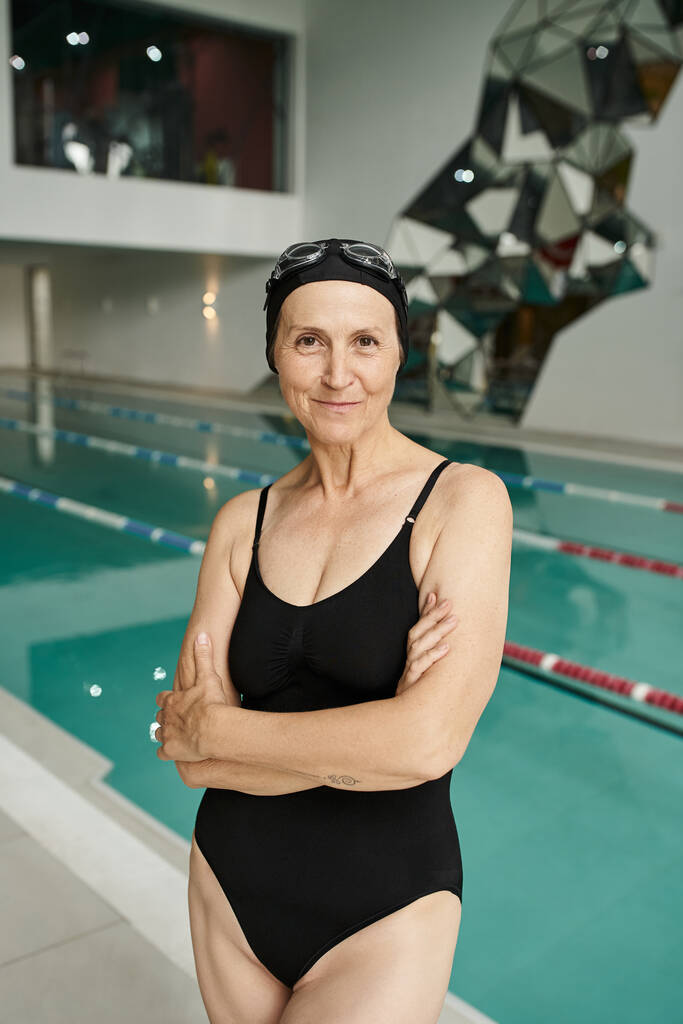 татуированная женщина средних лет в плавательной шапке и очках, бассейн в оздоровительном центре, сложенные руки - Фото, изображение
