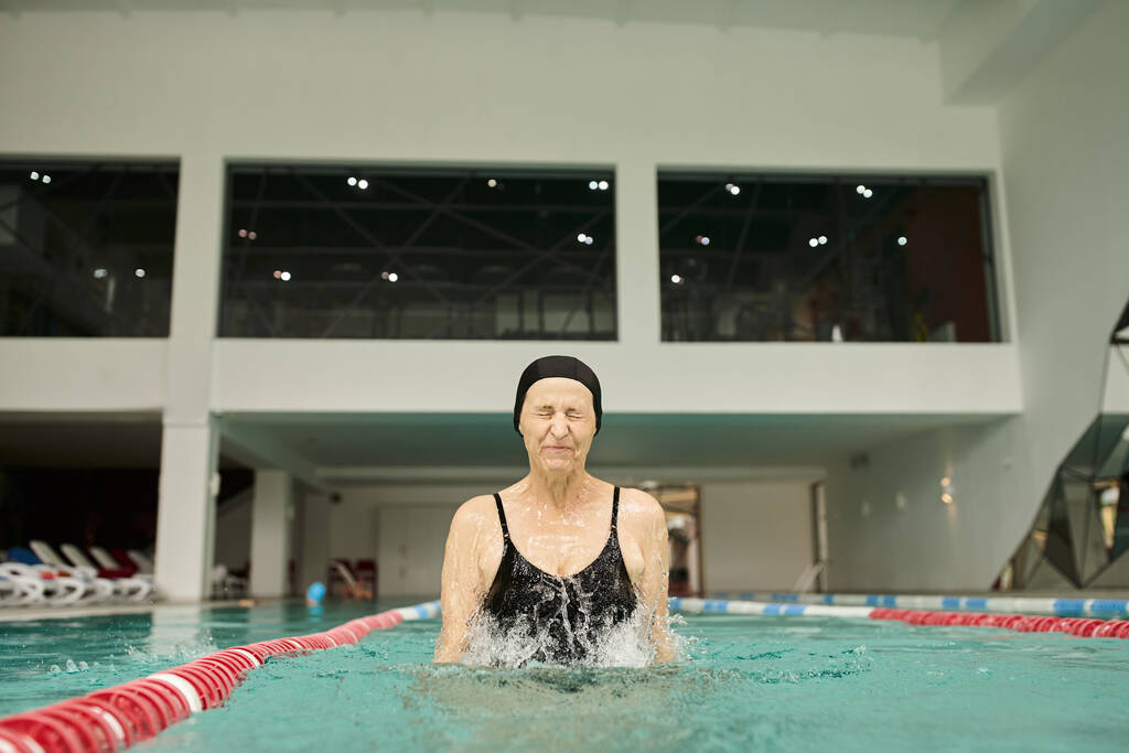 respingos de água, mulher madura em touca de natação e óculos se divertindo na piscina, olhos fechados, centro de spa - Foto, Imagem