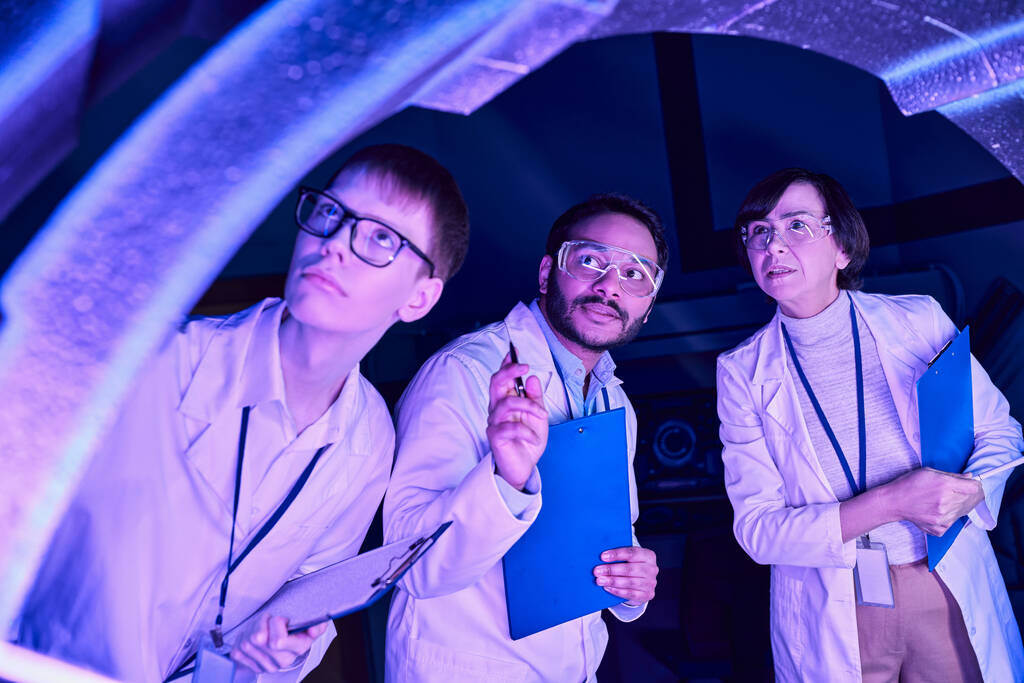 Futuristic Exploration: Diverse-Age Scientists Investigate Device in Neon-Lit Science Center - Photo, Image