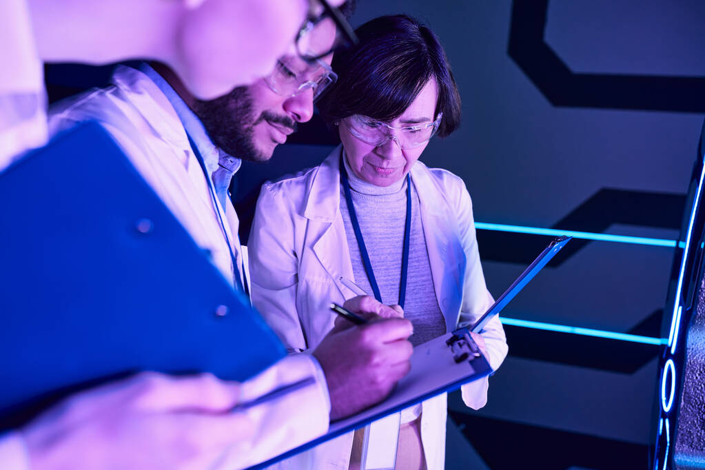 Φουτουριστική τεκμηρίωση: Τρεις επιστήμονες καταγράφουν τις παραμέτρους στο Neon-Lit Science Center - Φωτογραφία, εικόνα