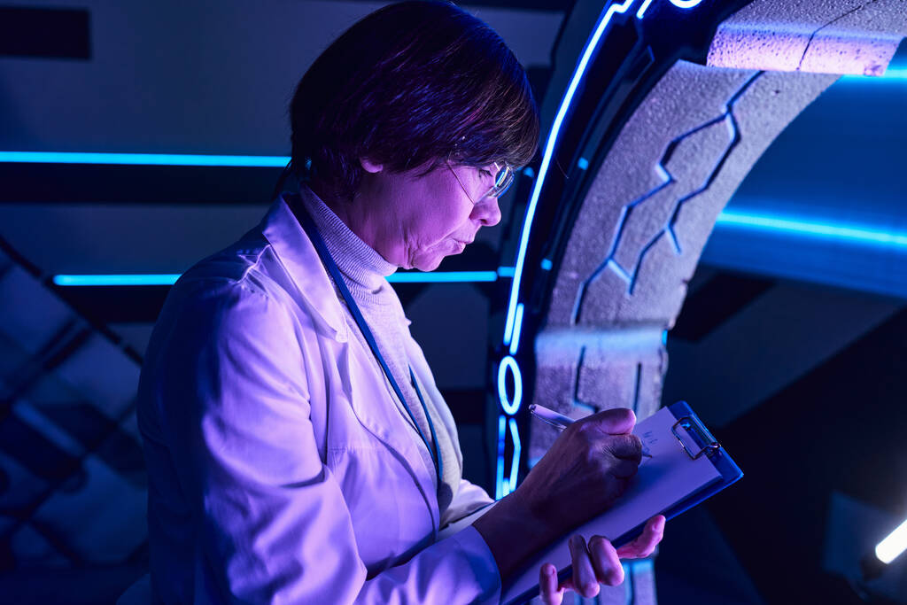 pesquisa futurista, experiente mulher cientista escrevendo em prancheta perto de novos equipamentos inovadores - Foto, Imagem