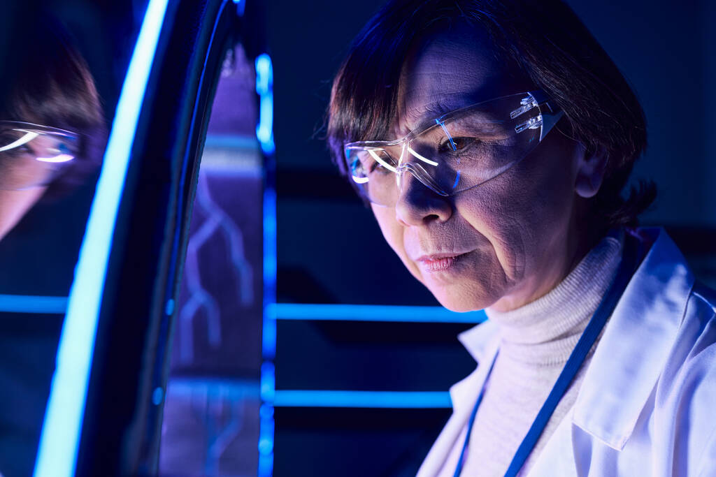 portrait of middle-aged woman scientist in goggles near new device in futuristic discovery center - Photo, Image