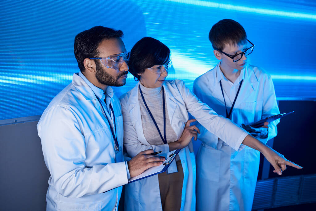 futuristisches Wissenschaftszentrum, Wissenschaftlerin zeigt mit dem Finger auf multiethnische Kollegen - Foto, Bild