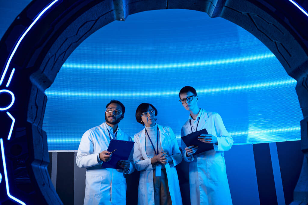 πολυεθνικοί επιστήμονες με πρόχειρο κοντά σε πειραματική συσκευή σε κόμβο καινοτομίας - Φωτογραφία, εικόνα