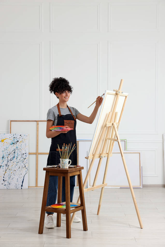 Молода жінка малює на мольберті з полотном в студії
 - Фото, зображення